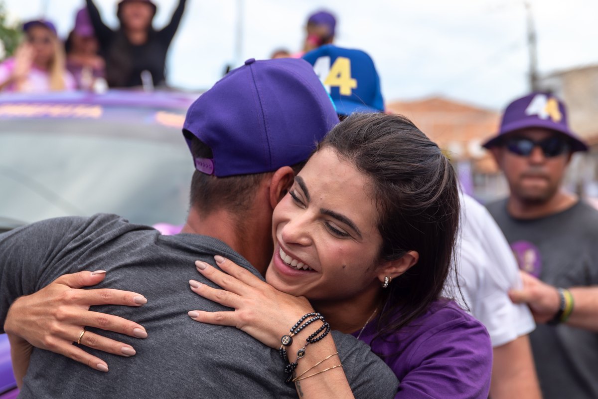 Yandra Moura abraçando um apoiador durante carreata, com o número 44 ao fundo